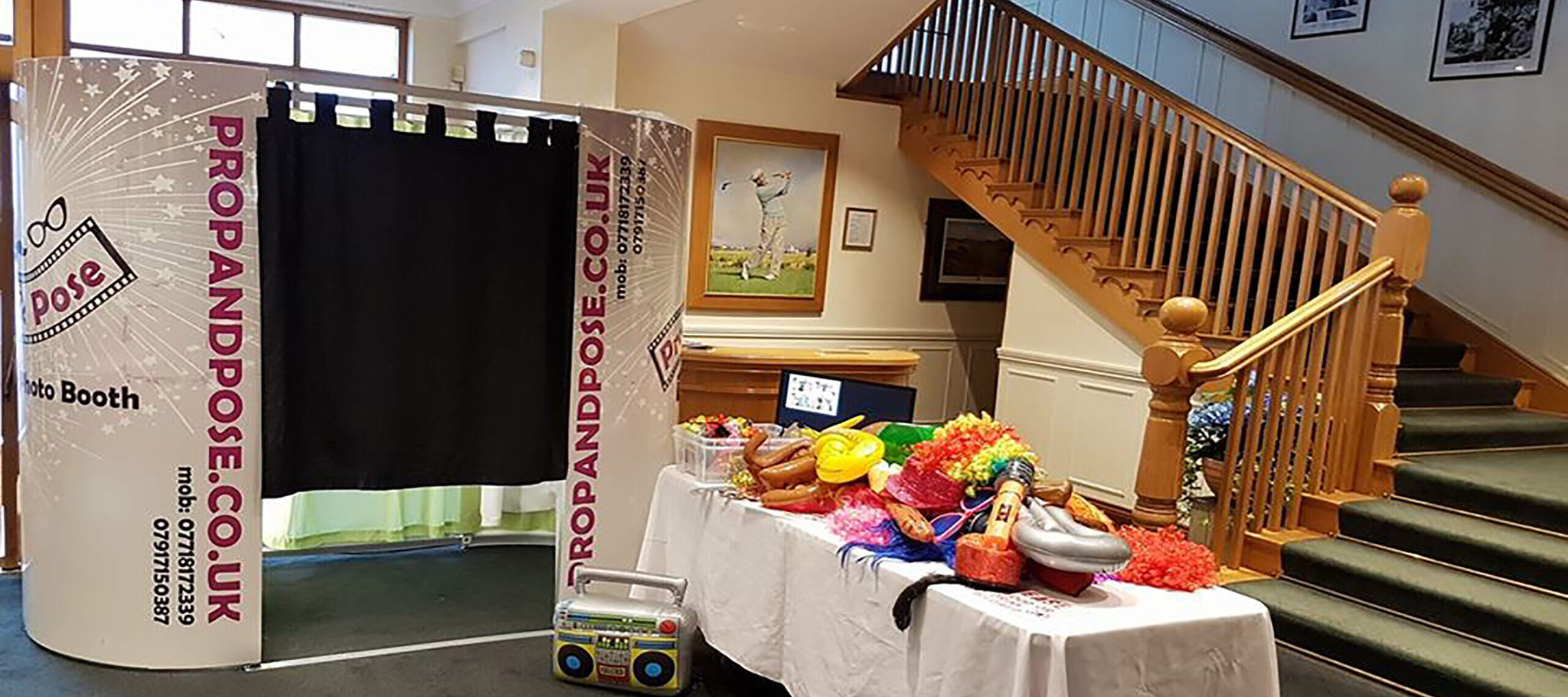 Photo booth setup with props table, colorful wigs, hats, and inflatable accessories.